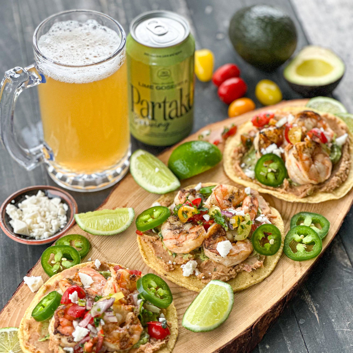 Tortillas with toppings, a glass of beer, and a can of Partake Brewing on a wooden board.
