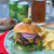Hamburger with toppings on a plate with chips and beer in the background