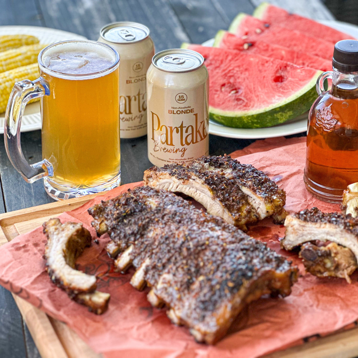 Outdoor setting with ribs, beer, and watermelon on a wooden table.