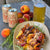 Grilled peach and chicken skewers served on a beige platter with rosemary, set on a rustic wooden table alongside Bartkoze Brewing peach beer cans and a glass of peach beer, with fresh peaches and rosemary sprigs.